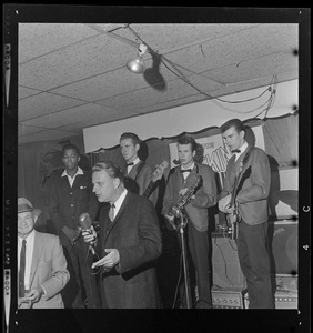 Evangelist Dr. Billy Graham takes to mike at a café in downtown Boston and speaks to patrons while the band looks on