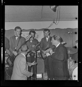 Evangelist Dr. Billy Graham takes to mike at a café in downtown Boston and speaks to patrons while the band looks on