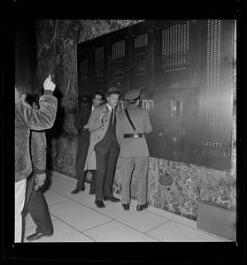 Security guard and two others in front of a panel in a lobby
