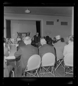 Man at a table addressing a seated audience