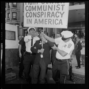 Police officers taking a sign from a protester that partially reads "Communist Conspiracy in America"