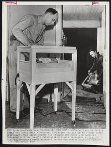 Portable Rig Saves Baby-The life of this child was saved when a portable generator was set up in a home here yesterday after sleet storms had knocked out power lines. Harold Furnish, (left) the baby's father, watches over incubator as Leo Parsels, consumers power mechanic checks the generator.