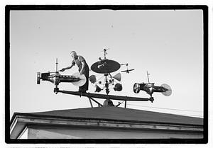 A man adjusting an elaborate device on roof, possibly a weather vane