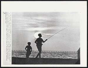 Silhouettes at Sunset -- Two young fishermen enjoy the sport the cool of the evening as they are silhouetted against the setting sun on Lake Pontchartrain in New Orleans. In the background is the 24-mile Lake Pontchartrain causeway, advertised as the longest bridge of it's kind in the world.