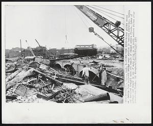 Rough Task Ahead- Worker guides crane as debris from railroad bridge near station is removed yesterday. Rubble and derailed freight cars are result of recent severe floods. Scene of salvage and repair is one of many going on in north eastern states after disastrous floods.