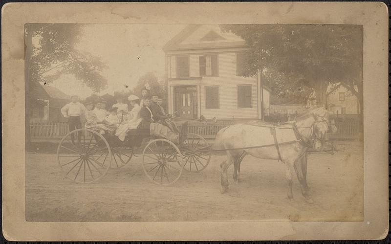 Carriage with group of people drawn by two horses in front of house