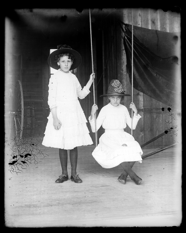 Two unidentified young women, one sitting on swing