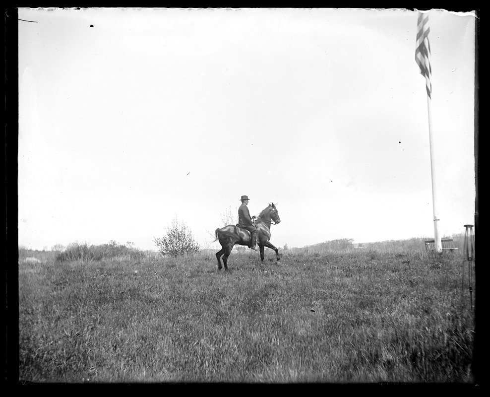 Unidentified man on horseback in field and flagpole
