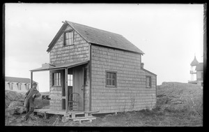 Man posing in front of small house or shed