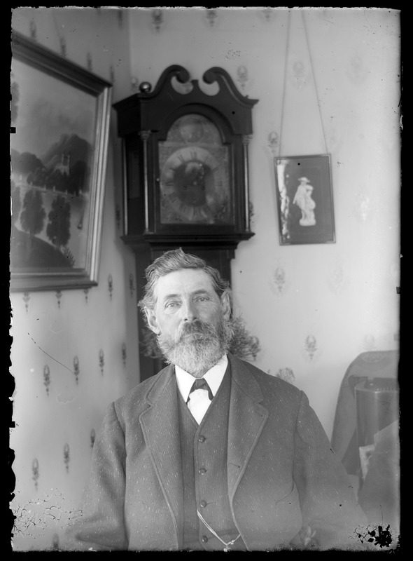 Unidentified man sitting in front of grandfather clcok