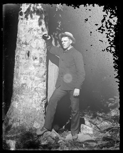 Unidentified man standing next to tree with many initials/name carvings