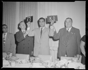 Rocky Marciano holds up new license plates that says "KO" while Governor Dever and Mayor Hynes look on