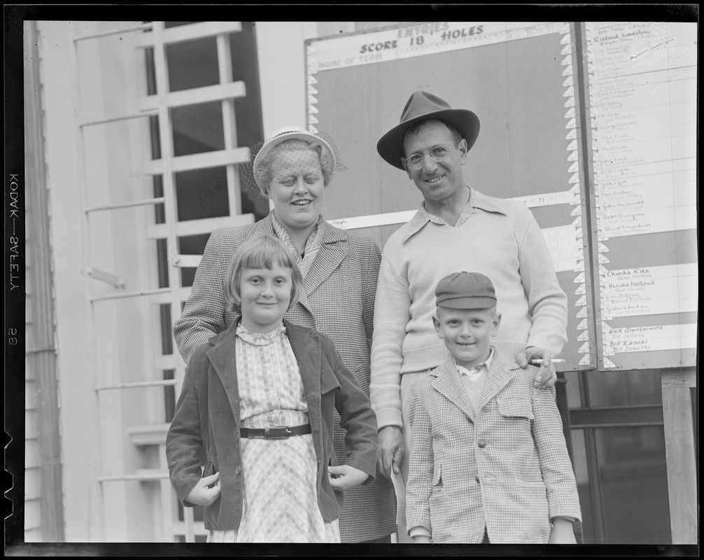 Man & woman and two children pose in front of scoreboard on clubhouse