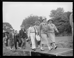 Women golfers and caddy walk over bridge on course