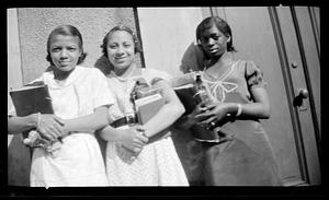 Three young women pose holding books in their arms