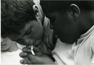 Two young boys lighting a cigarette from another cigarette