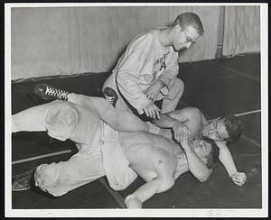 German Shell Made Him Coach, otherwise Howie Schless would be a Harvard varsity wrestler instead of Harvard freshman coach. Schless had his right shoulder shot away during the war and the doctors ordered him not to engage in competition, although he still works out with the freshman candidates. Here he is watching Pat Bowditch apply a body scissors to Len Gordon as the two try to be the 128-pound class representative.