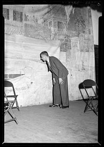 A man in suit bends over by a backdrop