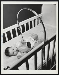 Makes Mothers Contented, Too -- A device invented by a Chicago advertising man relieves mother of holding the baby's bottle. Shayn Waddell, six-month-old daughter of Mr. and Mrs. William Waddell of Chicago, feeds from a bottle, which is enclosed in a plastic container.