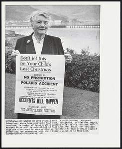 Leader in Anti-Polaris Move in Scotland – Mrs. Margaret Robertson, whose home overlooks Holy Loch, background, at Sandbank, Argyll, Scotland, is leader of local protest against base for U.S. nuclear submarines which will be established at Holy Loch next month. She displays sign she circulates in area calling on residents to sign petition against permitting the submarines with their Polaris missiles in Holy Loch.