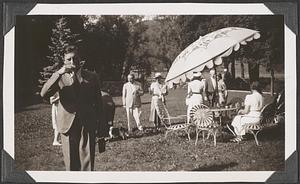 A group of people on a lawn, one woman sitting by an umbrella