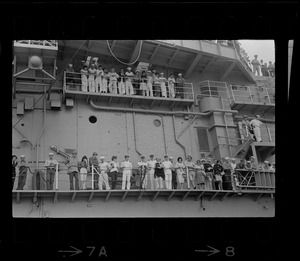 Sailors and passengers standing on ship's deck looking over railing