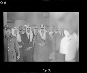 Blurry image of King Saud, an officer and other people wearing bisht over thawb