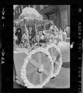 Girl holding onto decorated carriage filled with stuffed animals at Bunker Hill Day Parade