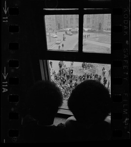 Two people looking at crowds through window during Boston College sit-in
