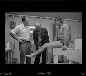 Boston College football player getting examined by trainer and Boston College football coach Joe Yukica standing by