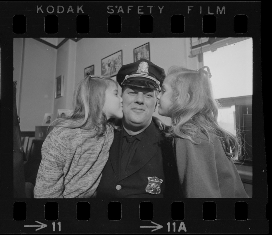 Happy about dad's promotion, Karyn, 8, and Cheryl, 6, use their father, Lieutenant Earl B. Crocker, as a target for kissing practice after ceremonies yesterday at Boston Police Headquarters