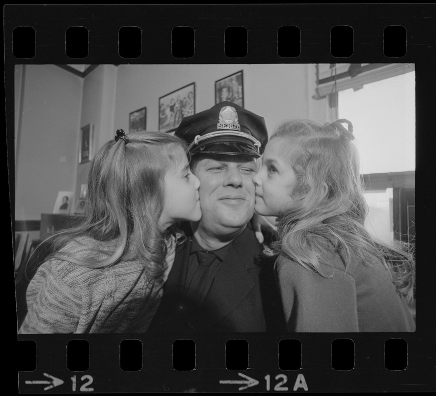 Happy about dad's promotion, Karyn, 8, and Cheryl, 6, use their father, Lieutenant Earl B. Crocker, as a target for kissing practice after ceremonies yesterday at Boston Police Headquarters