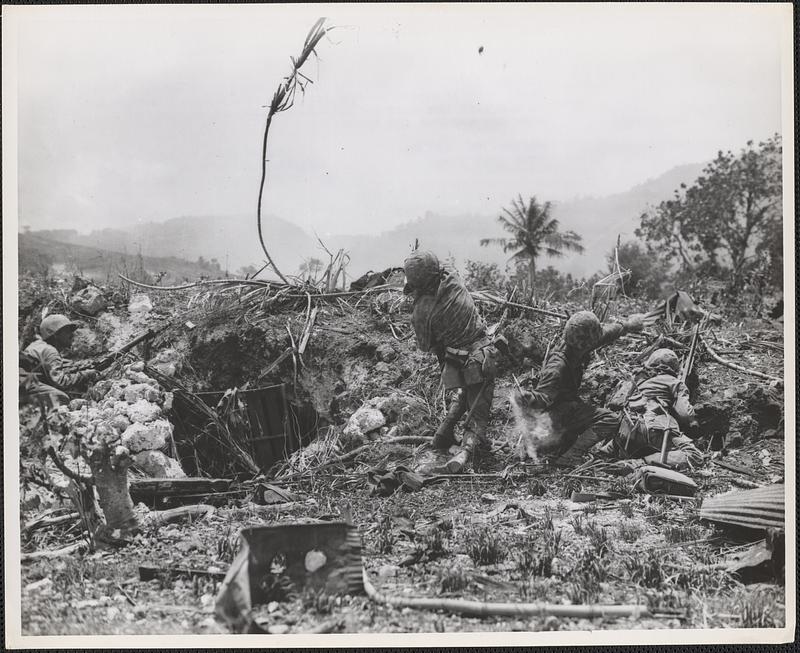 Marines on Saipan, protected by a small bank, lob grenades at the