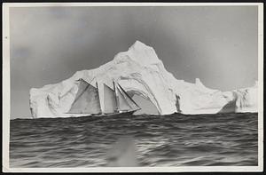 In The Frozen North With an Arctic Commuter. The Effie M. Morrissey passing close to a large berg to inspect the diversified formations more closely. The ship is passing on the weather side and a fresh wind is blowing. The ocean swell is heaving in on the berg. Behind the ship is a large hole in the berg.