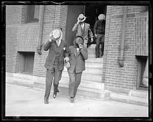 Four men walking out of a building covering their faces with their hats