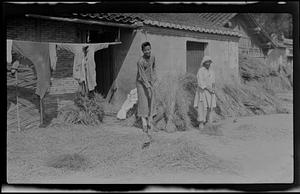 Two people cleaning in front of bundles of rice
