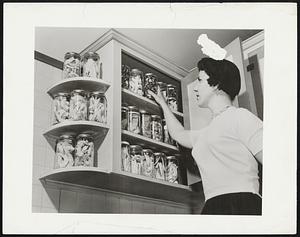 Food Stored At Room Temperature-- Wide variety of foods preserved in Raytheon Manufacturing Company's food laboratory, can be stored one kitchen shelf indefinitely at room temperature. In photo, Pat McGovern reaches for a jar of strawberries on pantry shelf. Other preserved foods on top shelf inside cupboard are--left to right--lobster tails, shrimp, filet of sole and strawberries (small jar on top) and shrimp beneath. Second shelf holds--left to right--chicken breasts, veal, sirloin steak, mushrooms and steak, Bottom shelf and those outside cabinet are laden with shrimp.