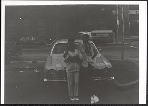 A young man and woman posing in front of a car
