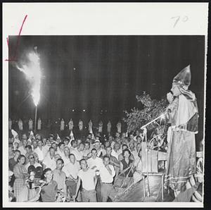 Several Thousand People listen to C.H. Maddox of Savannah, Ga., as a cross burns in background during a rally by the Ku Klux Klan in a pasture just outside city limits of Albany Ga., last night. Grand Dragon Calvin Craig said the Klan was launching "the biggest drive ever known in the state of Georgia and when we get through I think there'll be a lot of Negroes moving north."
