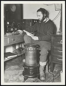 Cold Weather, Warm Feet. With his feet planted next to an oil stove, Benjamin Schiffer sends out his daily weather report over shortwave radio to Albany Airport. This radio is the overservers' only communication with the outside world during most of the winter. Seven months food supply was taken to the mountain top last fall. Water is obtained by melting ice and snow. Electricity is used for cooking, coal and oil for heating in the snow-bound post.