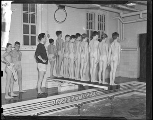 Row of naked boys stand on diving board at indoor pool