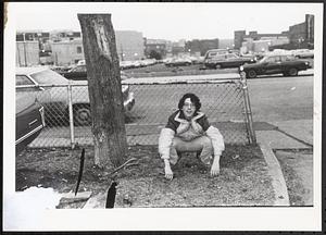 Young man crouching in front of a fence