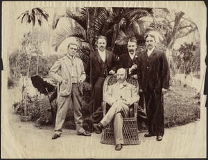 Five men posing in front of palm trees; one balding man sitting in wicker chair, JGC on far right