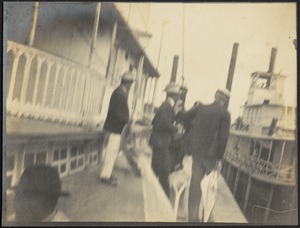 Well-dressed men with straw hats standing near boat (possibly a paddleboat)