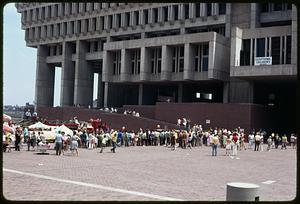 A crowd of people on Boston City Hall plaza, fire truck in background