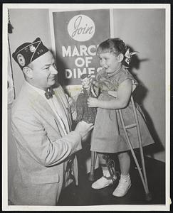 Dolly Helps -- Laurelie Topliffe, 3, gets help in pinning "Blue Crutch Pin" on her dolly from William Sloane, Legion chairman for drive beginning on Thursday.