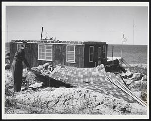 Easy to Handle, the roof that formerly covered the cottage in the background at 15A Stony Beach Rd., Hull, is inspected by Miss Mary Sullivan of Dorchester.