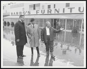 Three men stand by flooded street, Barbo's Furniture store in background