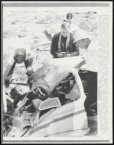 As police chaplain Fr. Peter Rogers gives the last rites, fire officials look over the small plane carrying four, including a doctor, that crashed and burned on takeoff at Lakefron Airport 8/19 killing all aboard. The plane was destined for hurricane ravaged Gulfport, Miss. with penicillin and other medical supplies.