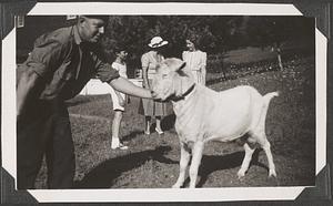 A man petting a goat, three unidentified people in background